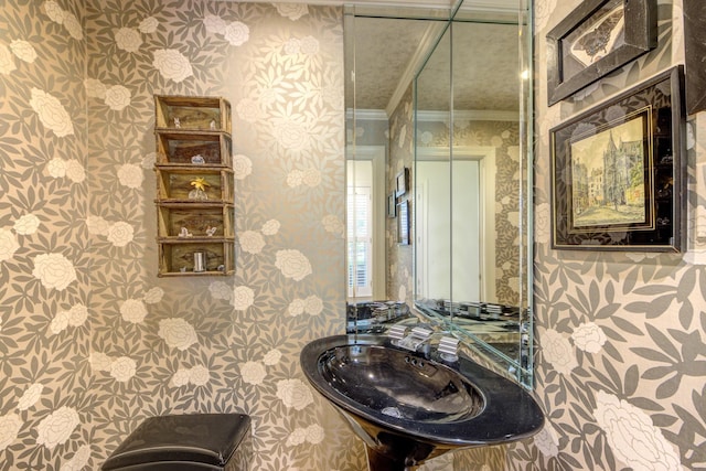 bathroom with wallpapered walls, crown molding, and a sink