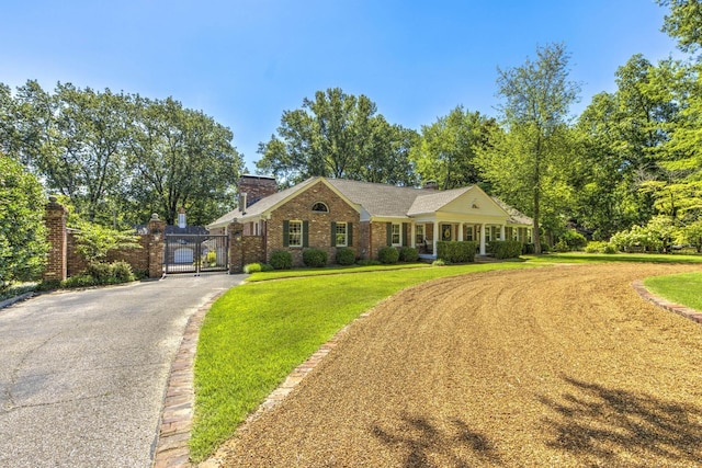 view of front of house featuring brick siding, aphalt driveway, a front yard, a chimney, and a gate