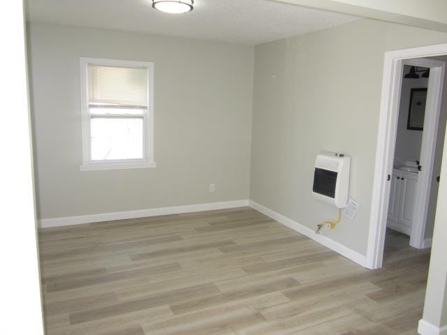 empty room with heating unit, light wood finished floors, and baseboards