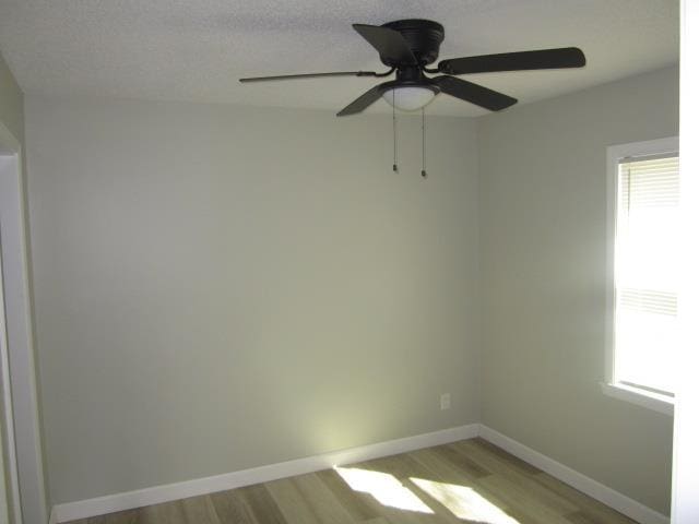 empty room featuring light wood finished floors, ceiling fan, a textured ceiling, and baseboards