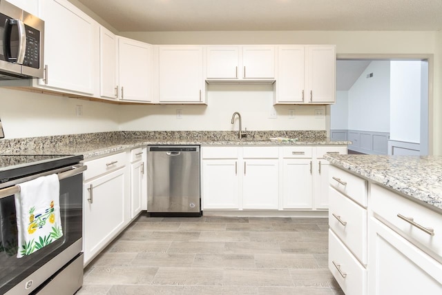 kitchen featuring white cabinets, appliances with stainless steel finishes, light wood-style flooring, and a sink