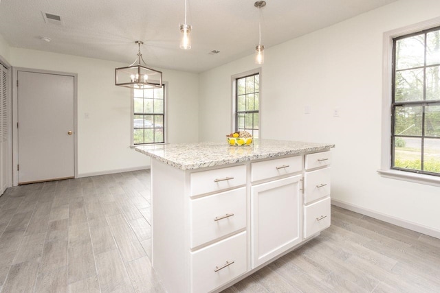 kitchen featuring visible vents, a center island, decorative light fixtures, light wood-style flooring, and white cabinets