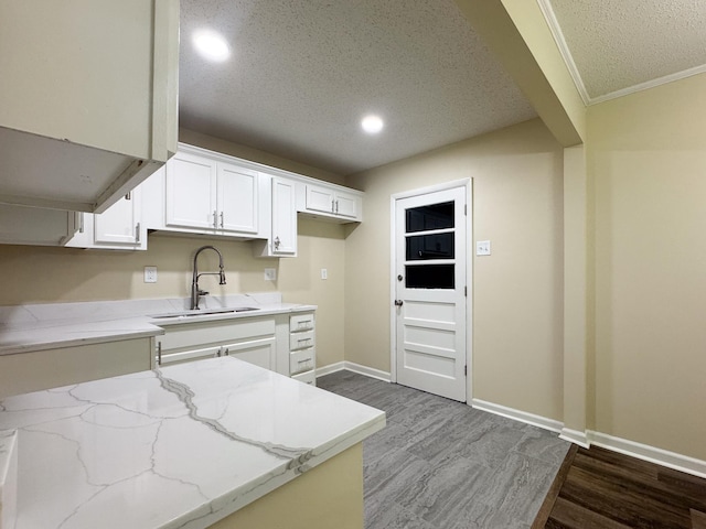 kitchen with baseboards, light stone countertops, wood finished floors, white cabinetry, and a sink