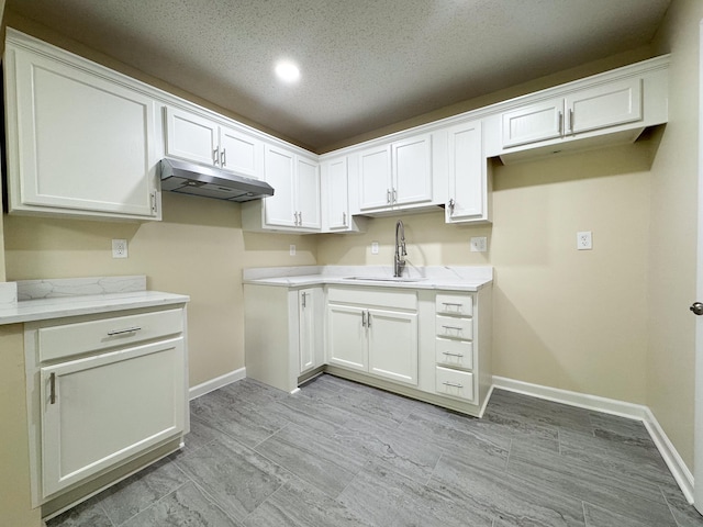 kitchen featuring under cabinet range hood, white cabinets, baseboards, and a sink