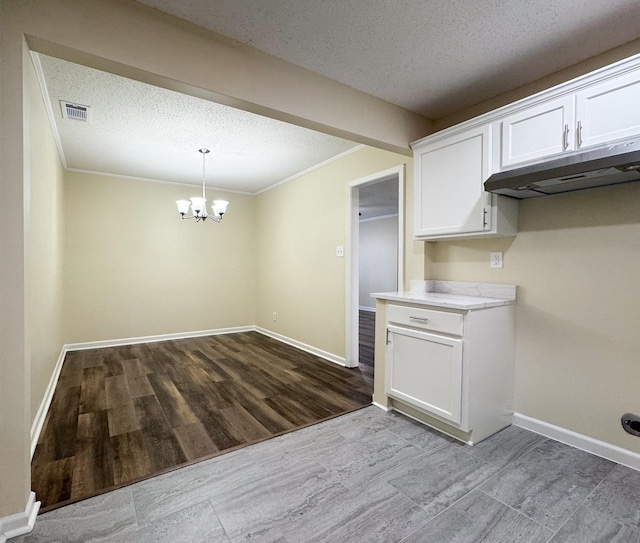 kitchen featuring visible vents, an inviting chandelier, light countertops, under cabinet range hood, and white cabinetry