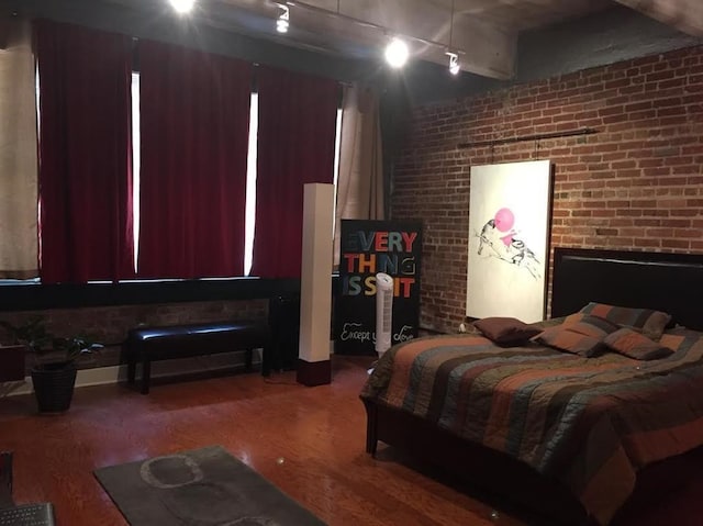 bedroom featuring rail lighting, wood finished floors, and brick wall