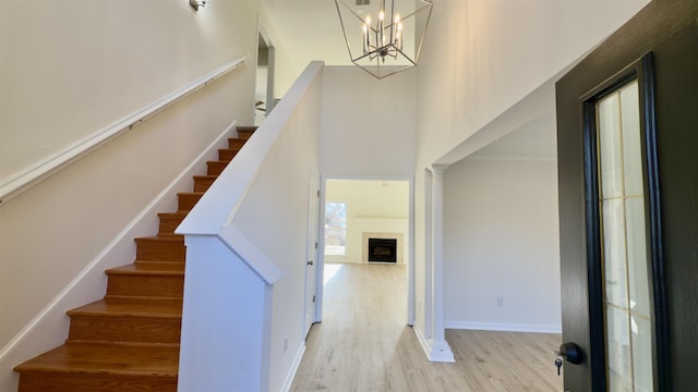 stairway featuring wood finished floors, baseboards, a fireplace, a towering ceiling, and a notable chandelier