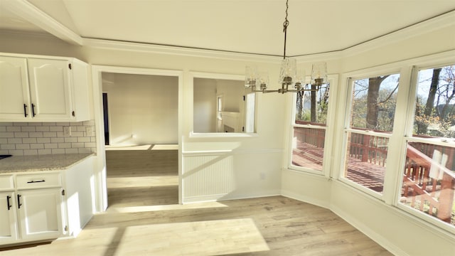 unfurnished dining area featuring baseboards, light wood-type flooring, an inviting chandelier, and ornamental molding