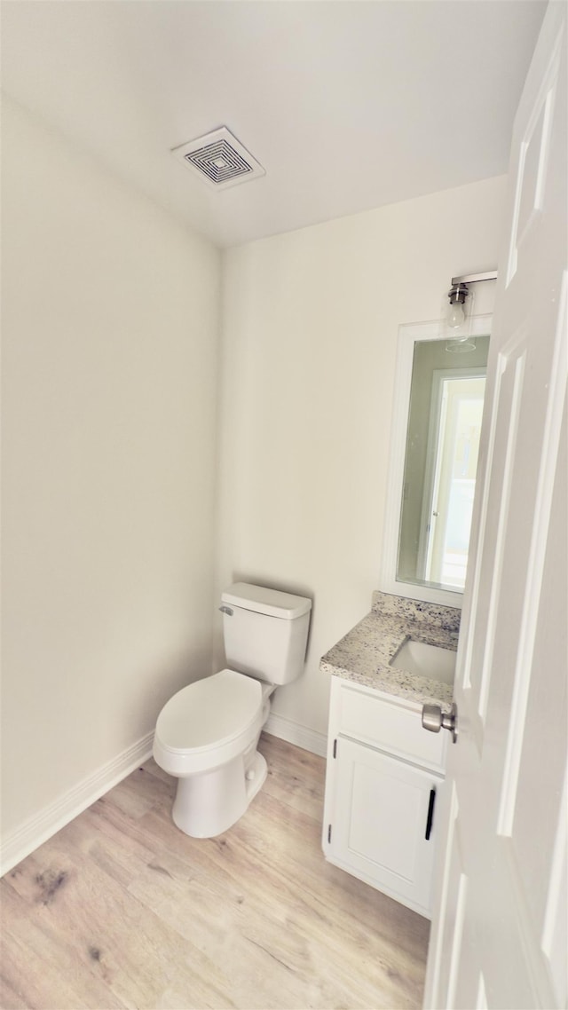 half bathroom with vanity, wood finished floors, visible vents, baseboards, and toilet