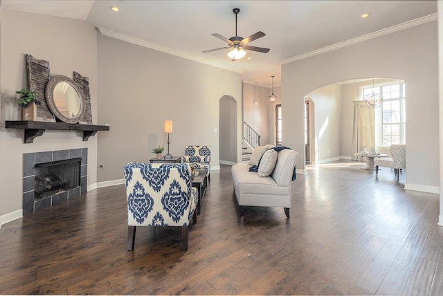 living room with wood finished floors, baseboards, arched walkways, stairs, and a tiled fireplace