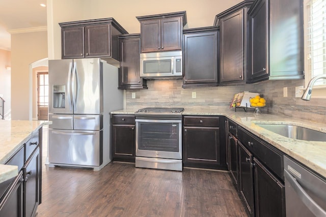 kitchen with light stone countertops, a sink, decorative backsplash, dark wood-type flooring, and stainless steel appliances