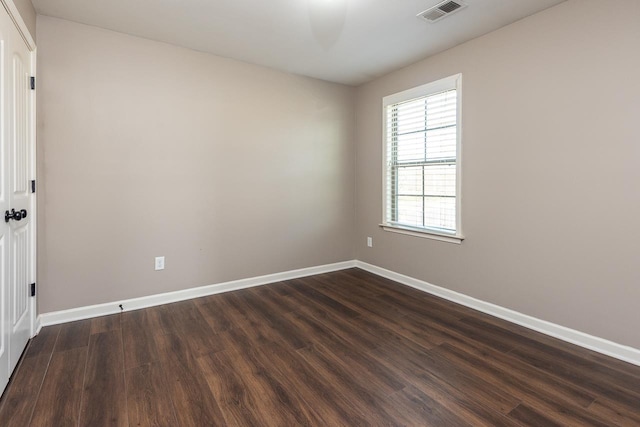 empty room featuring dark wood finished floors, visible vents, and baseboards