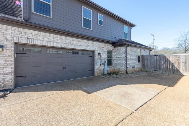 view of home's exterior featuring brick siding, driveway, an attached garage, and fence