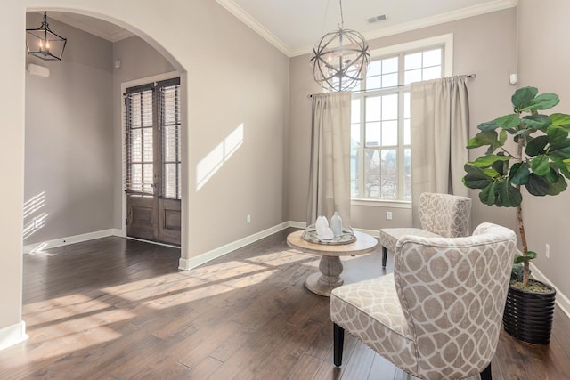 living area with a healthy amount of sunlight, ornamental molding, an inviting chandelier, arched walkways, and dark wood-style flooring