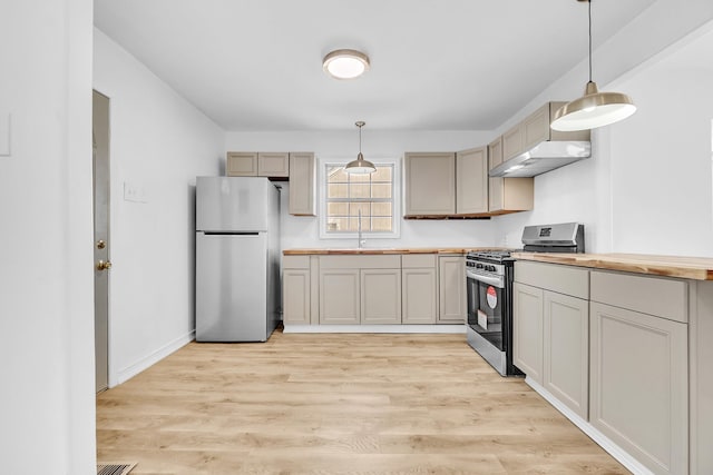 kitchen featuring under cabinet range hood, light wood-type flooring, appliances with stainless steel finishes, hanging light fixtures, and a sink