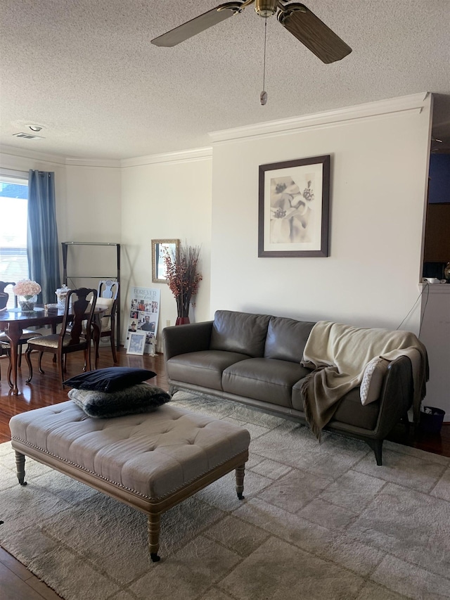 living room with a textured ceiling, wood finished floors, ceiling fan, and ornamental molding