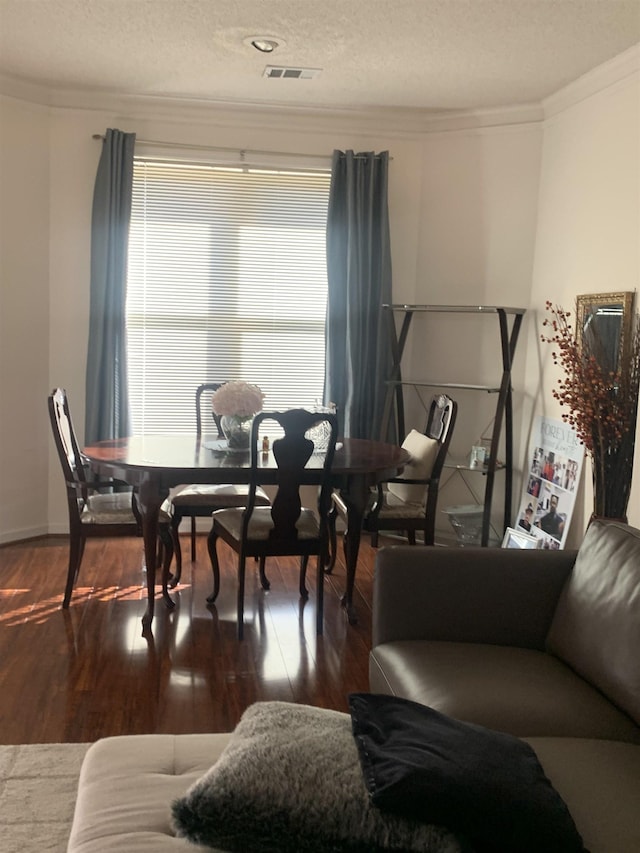 dining space with visible vents, a textured ceiling, wood finished floors, and ornamental molding