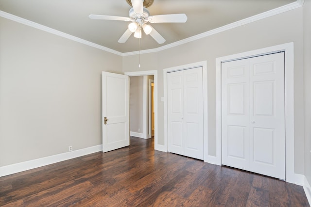 unfurnished bedroom featuring two closets, dark wood-type flooring, ornamental molding, a ceiling fan, and baseboards