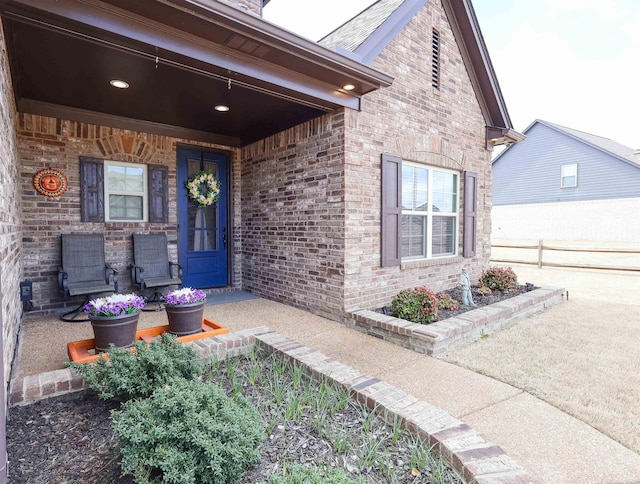 property entrance with brick siding, a porch, and fence