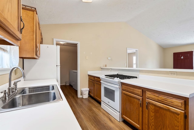 kitchen with a sink, wood finished floors, white appliances, brown cabinetry, and lofted ceiling