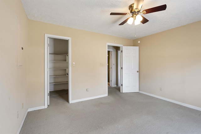 unfurnished bedroom with a walk in closet, baseboards, a textured ceiling, and light colored carpet