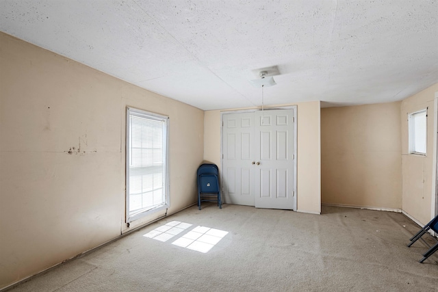 unfurnished bedroom featuring carpet flooring, multiple windows, and a textured ceiling