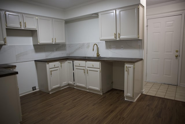 kitchen featuring dark wood-type flooring, ornamental molding, a sink, tasteful backsplash, and dark countertops