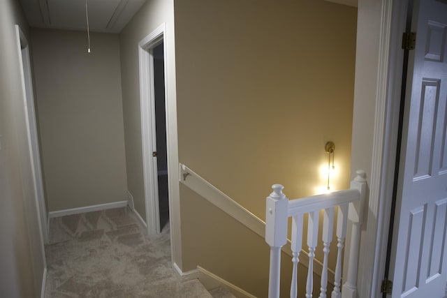 hall featuring an upstairs landing, attic access, baseboards, and carpet floors