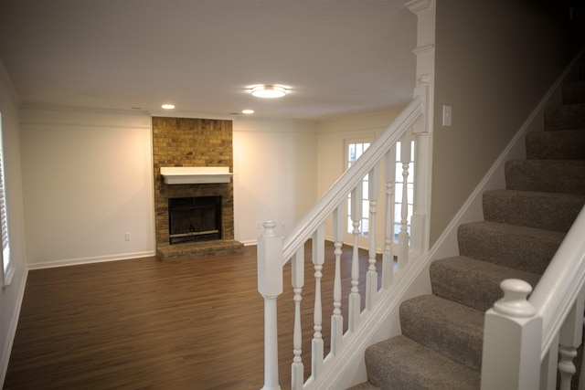 staircase featuring ornamental molding, a fireplace, baseboards, and wood finished floors