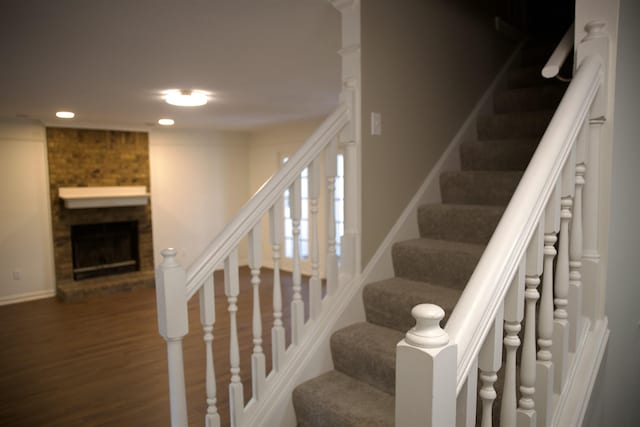 staircase with a brick fireplace, recessed lighting, and wood finished floors