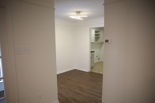 hallway featuring dark wood-style flooring, a textured ceiling, baseboards, and ornamental molding