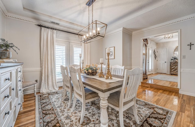 dining space featuring light wood-type flooring, a notable chandelier, ornamental molding, and a textured ceiling