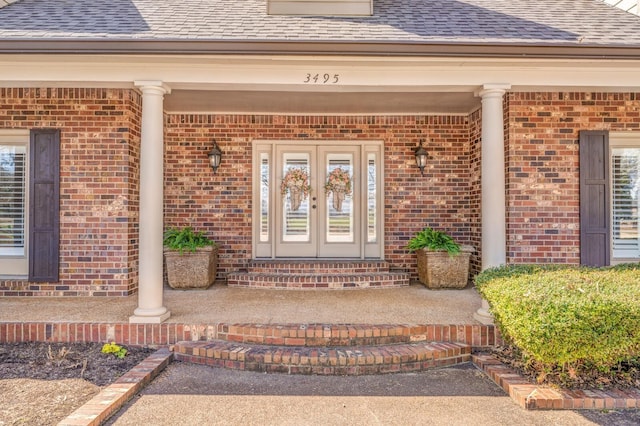 property entrance with covered porch, french doors, brick siding, and a shingled roof