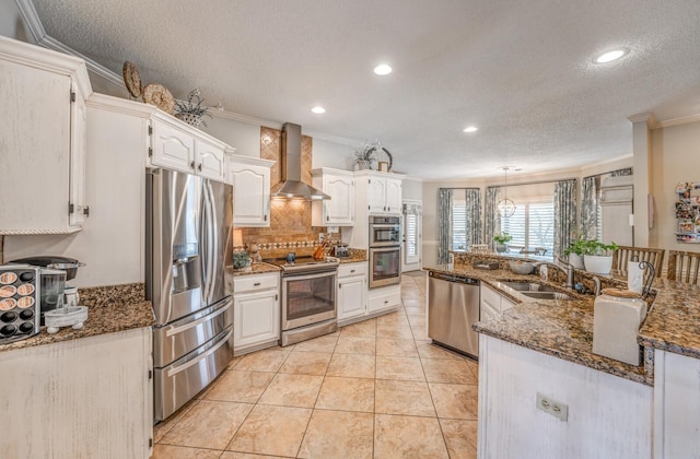 kitchen with wall chimney range hood, ornamental molding, white cabinets, stainless steel appliances, and a sink