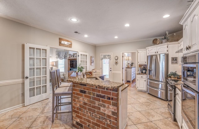 kitchen with visible vents, a sink, dark stone counters, appliances with stainless steel finishes, and white cabinets