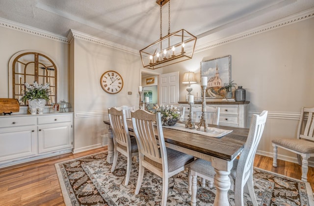 dining space with crown molding, a notable chandelier, light wood-type flooring, and a textured ceiling