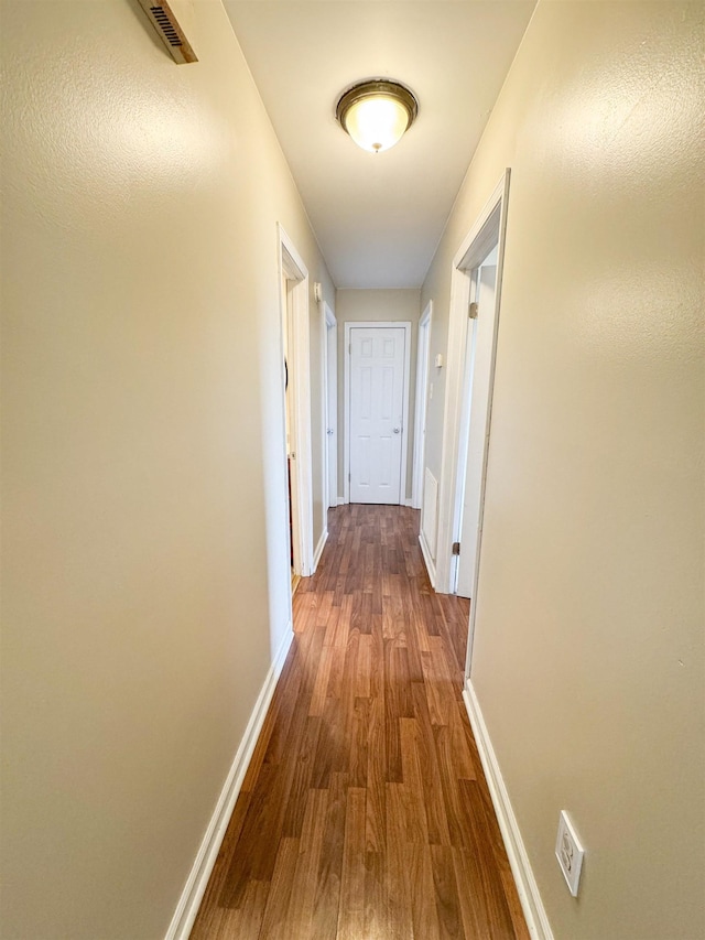 corridor featuring visible vents, baseboards, and dark wood-style flooring