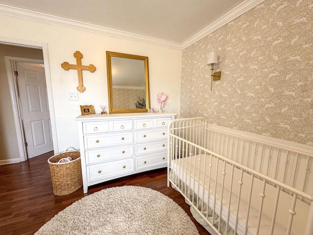 bedroom featuring a wainscoted wall, a crib, dark wood-style floors, crown molding, and wallpapered walls