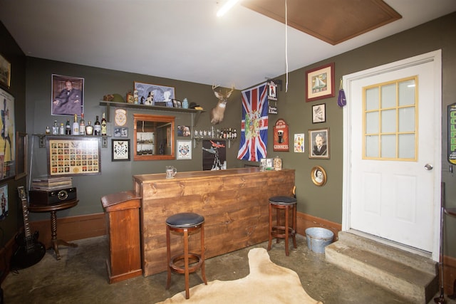 bar with a bar, unfinished concrete floors, and baseboards