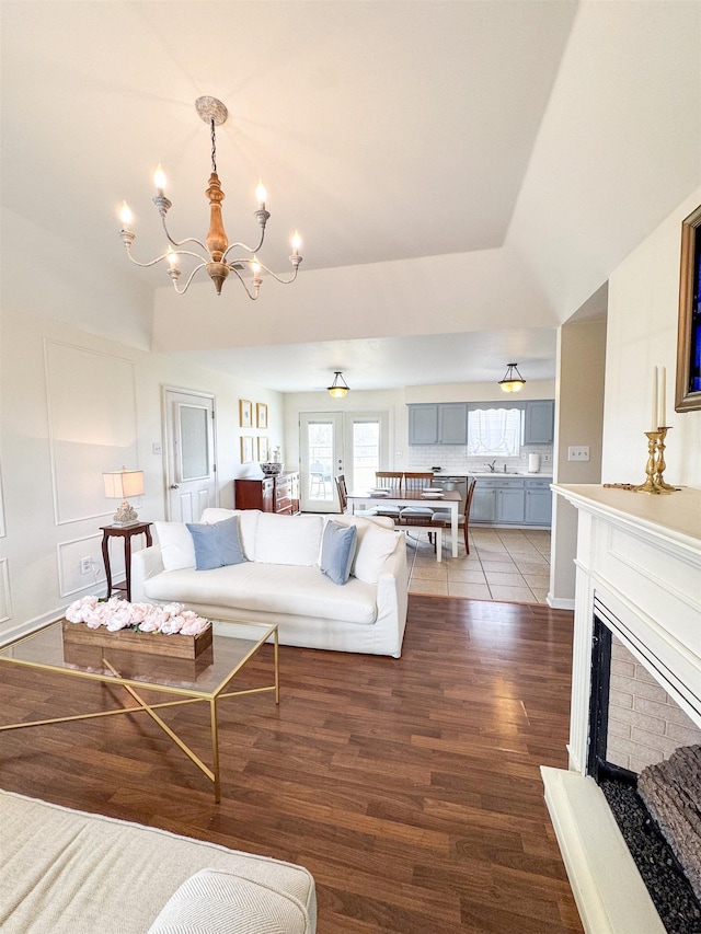 living room with a chandelier, a decorative wall, a fireplace with raised hearth, and wood finished floors