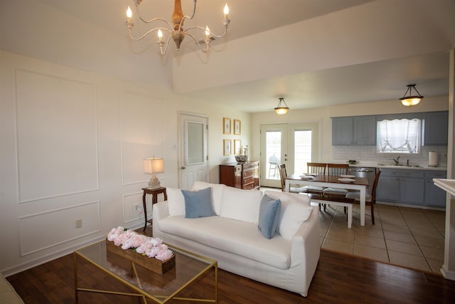 living area featuring an inviting chandelier, a decorative wall, dark wood-style floors, and french doors