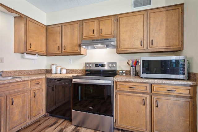 kitchen with visible vents, brown cabinets, under cabinet range hood, a sink, and stainless steel appliances