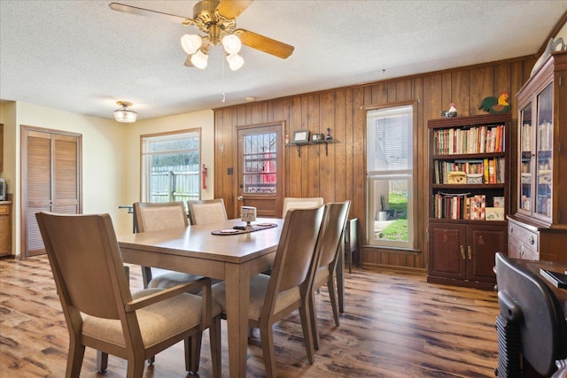 dining space featuring a textured ceiling, wood finished floors, wood walls, and ceiling fan