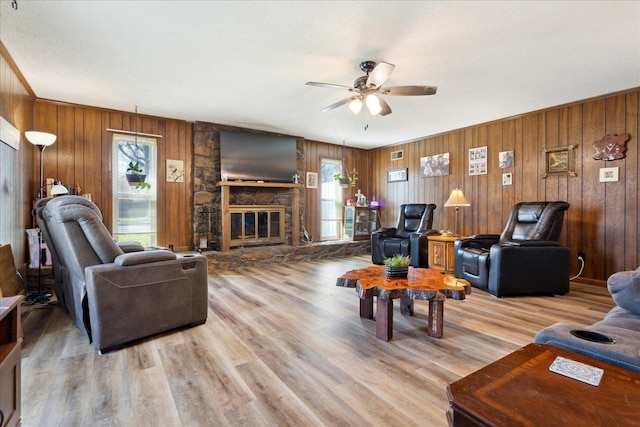 living area with a ceiling fan, visible vents, light wood-style flooring, a fireplace, and wood walls