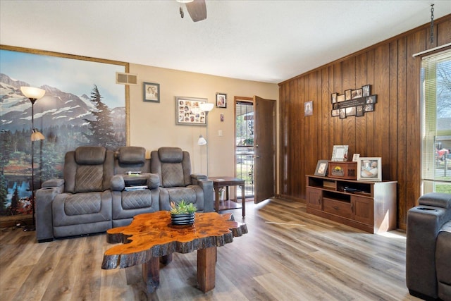 living room featuring visible vents, wood walls, light wood-type flooring, and ceiling fan