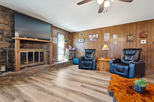 unfurnished living room with visible vents, ceiling fan, wood walls, a stone fireplace, and wood finished floors