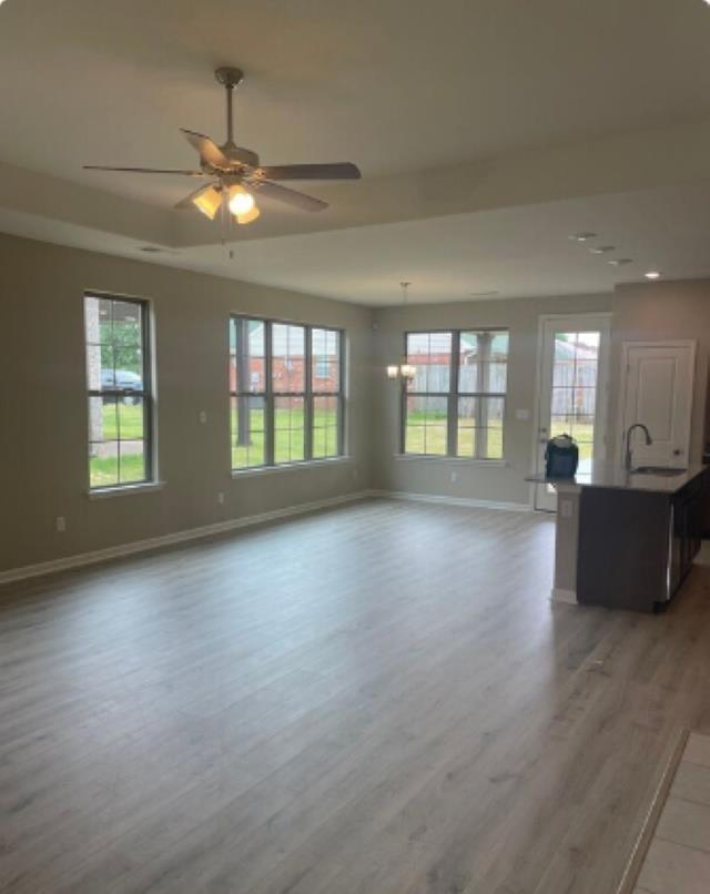 unfurnished living room with plenty of natural light, baseboards, a ceiling fan, and wood finished floors