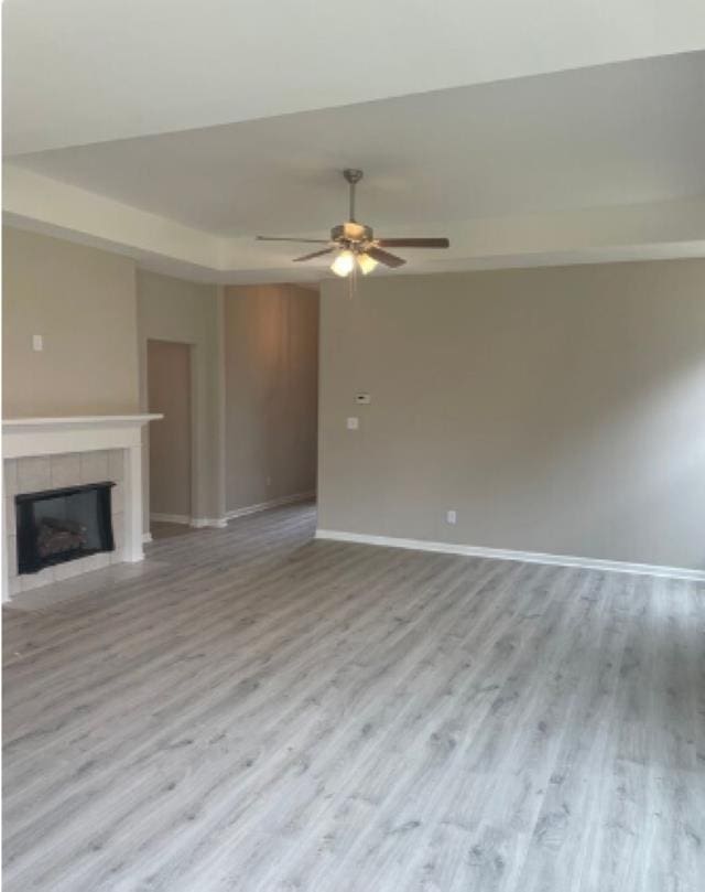 unfurnished living room with wood finished floors, a fireplace, baseboards, and ceiling fan