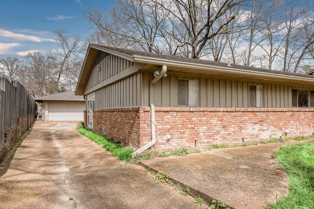 view of side of home featuring fence, an outdoor structure, a garage, board and batten siding, and brick siding