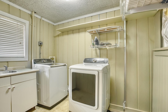 clothes washing area with ornamental molding, a sink, a textured ceiling, washing machine and dryer, and cabinet space